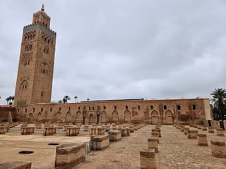 Meczet koutoubia w marrakeszu z charakterystycznym minaretem i rozległym dziedzińcem pod pochmurnym niebem