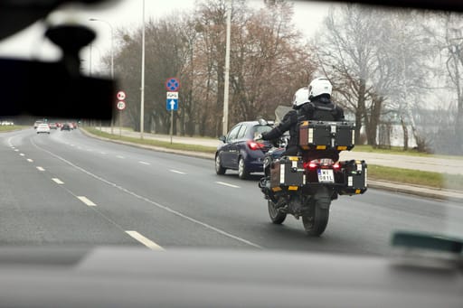 Dwóch motocyklistów jedzie ulicą w warszawie, z kuframi i białymi kaskami.