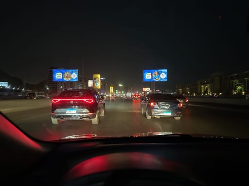 Nocny ruch na alei safety w egipcie, widziany z samochodu, z reklamami i światłami aut.