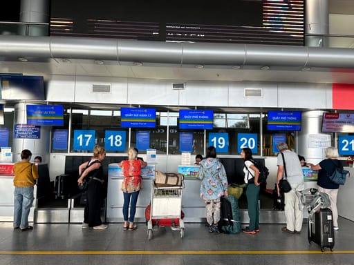 Pasażerowie przy stanowiskach odprawy bagażu na lotnisku, z walizkami i wózkiem bagażowym