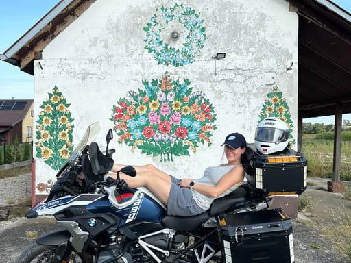 Rowerzystka na motocyklu przed malowaną kwiatami chatą w zalipiu.