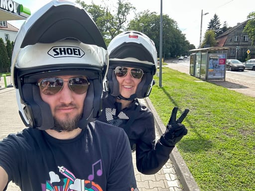 Dwoje motocyklistów w kaskach robi selfie przy przystanku w szczecinie.