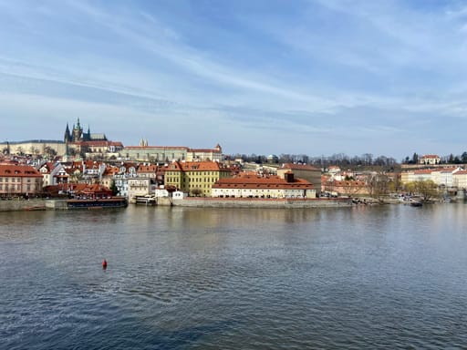 Panorama pragi nad wełtawą z zamkiem praskim i czerwonymi dachami.