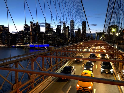 Most brookliński w nowym jorku z ruchem samochodowym i panoramą manhattan o zmierzchu