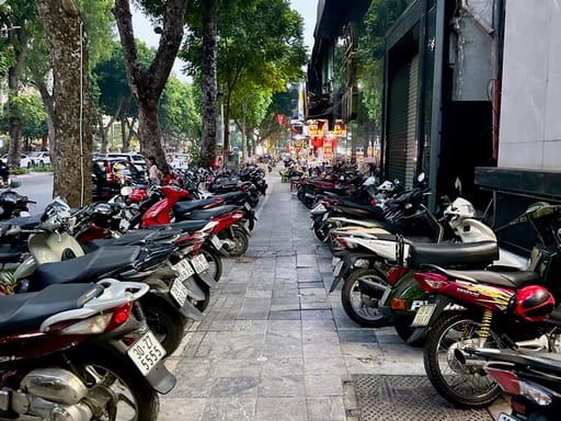 Ulica w hanoi zastawiona zaparkowanymi skuterami przy chodniku i drzewach.