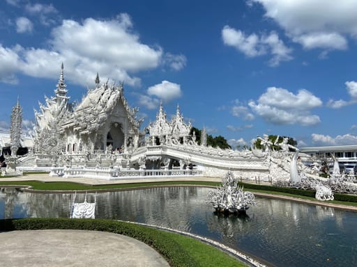 Biała świątynia wat rong khun w chiang rai, odbijająca się w stawie pod błękitnym niebem.