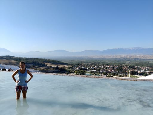 Kobieta stoi w białych tarasach pamukkale z panoramą doliny w tle.