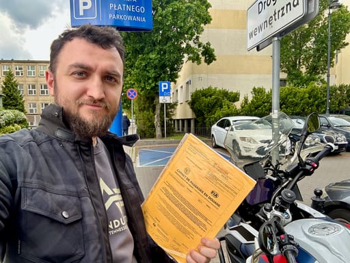 Mężczyzna z motorem trzyma carnet de passage na ulicy w warszawie.