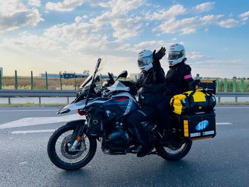 Dwoje motocyklistów na turystycznym motocyklu na trasie w desert horizons, jedno macha do kamery.
