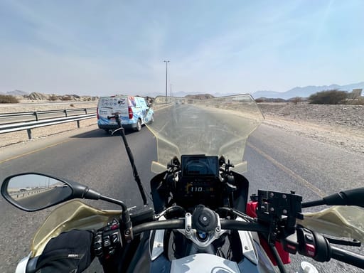 Widok z motocykla na pustynną drogę w omanie, z vanem przed sobą.