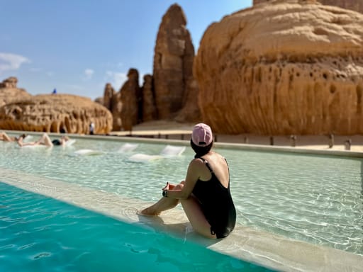 Kobieta siedząca w basenie w habitas al ula w arabii saudyjskiej, na tle monumentalnych piaskowcowych skał