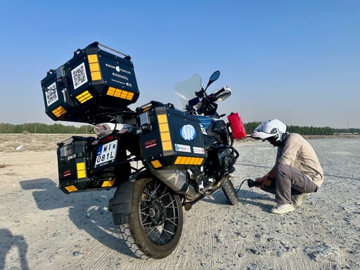 Filip z motocyklem turystycznym na szutrowym postoju w dubaju, pompuje koło w kasku i jasnym ubraniu