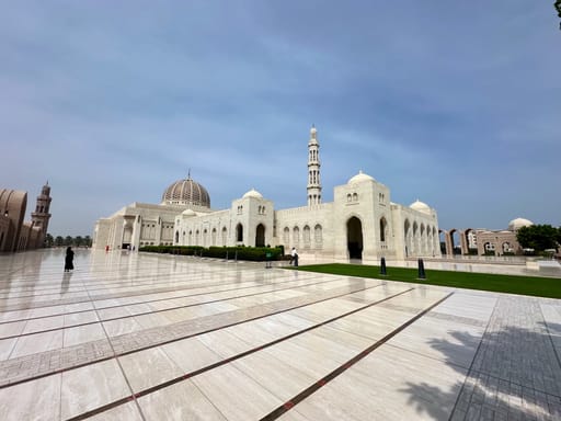 Wielki meczet w maskacie w omanie, biały kompleks z kopułą i wysokim minaretem przy rozległym dziedzińcu.