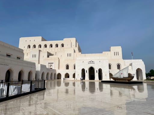 Royal opera house muscat w omanie, jasny gmach z arkadami i łodzią na dziedzińcu po deszczu