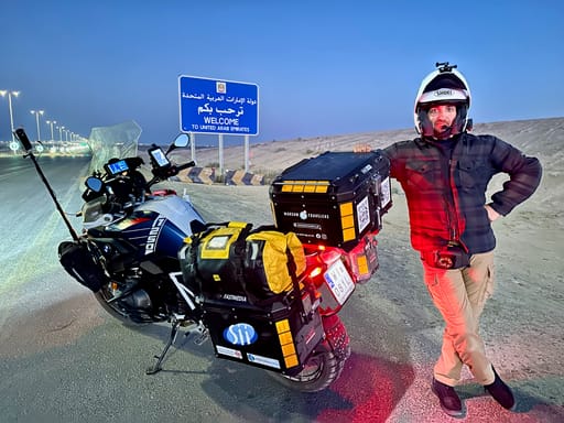 Motocyklista z wyprawowym bmw przy znaku al ghuwaifat land border witającym w zjednoczonych emiratach arabskich