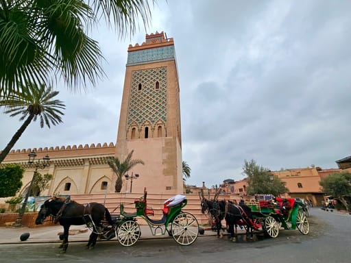 Bab al qsar w marrakeszu, wysoka wieża z dekoracyjną fasadą i konne dorożki na ulicy.