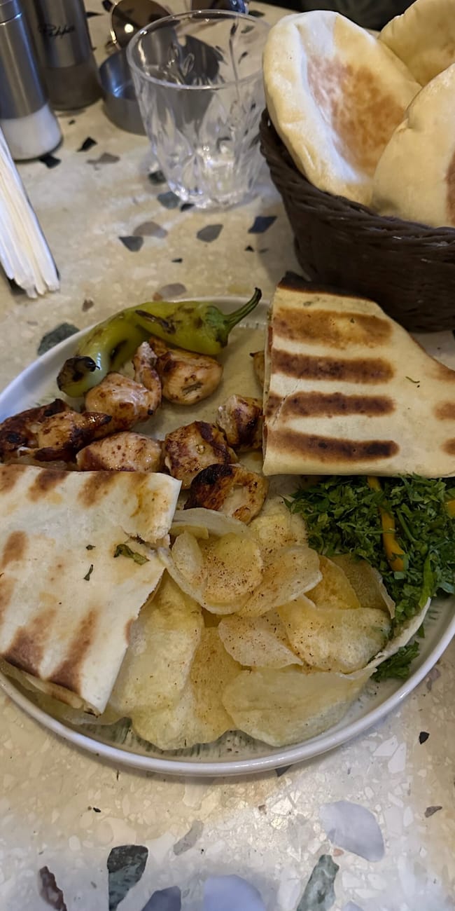 Egyptian food platter with grilled chicken, flatbread, chips, and herbs