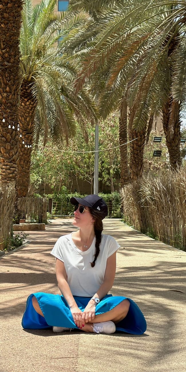 Kobieta siedzi na ścieżce wśród palm w arabii saudyjskiej, patrząc w bok.