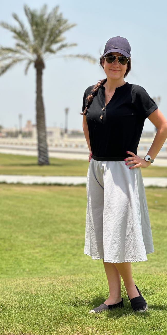 Kobieta stoi na trawniku przy dammam corniche w arabii saudyjskiej, z palmą w tle.