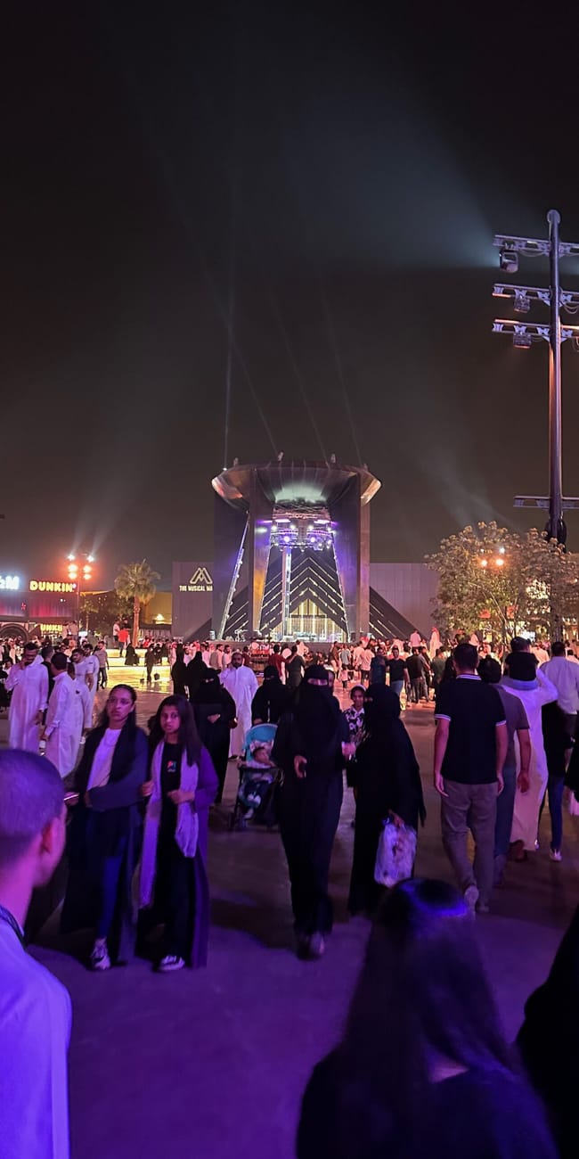 Tłumy spacerują nocą po riyadh boulevard world przy podświetlonej scenie i budynkach.
