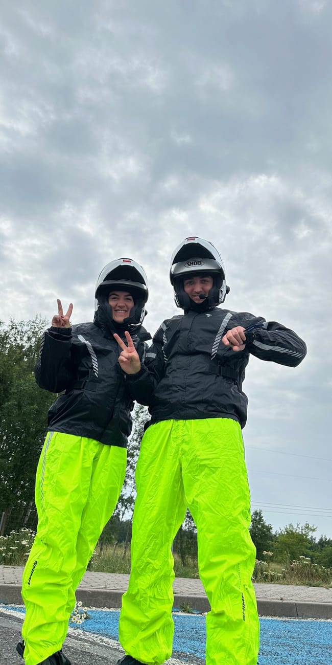 Dwoje motocyklistów w kaskach i jaskrawożółtych spodniach przeciwdeszczowych w niemczech, pozujący na postoju.