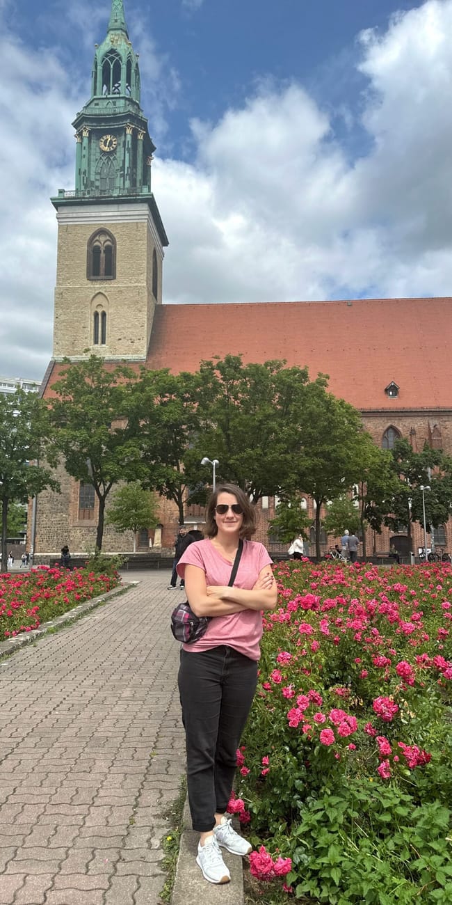 Berlin marienkirche z wieżą, przed którą stoi kobieta wśród różowych kwiatów.