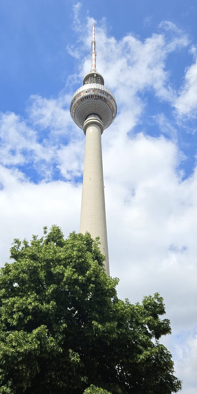 Berliński fernsehturm nad drzewami na tle nieba z chmurami