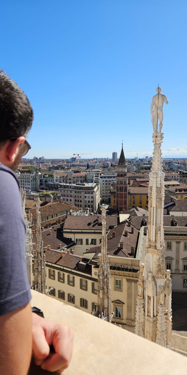Widok z dachu duomo w mediolanie na miasto i wieże katedry, z mężczyzną na pierwszym planie