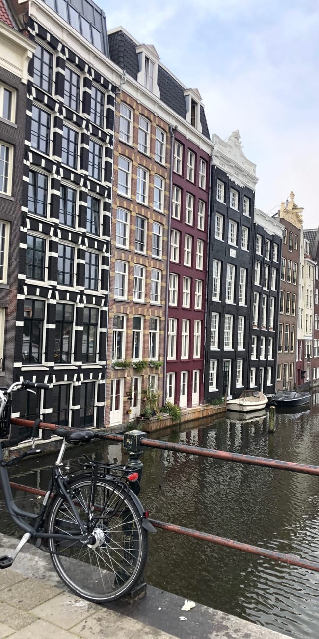 Kanał w amsterdamie z wąskimi kamienicami i rowerem na moście