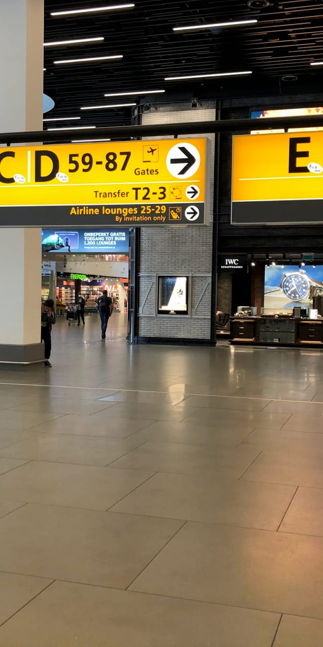 Hol na lotnisku amsterdam airport z żółtymi znakami kierującymi do bramek i transferów.