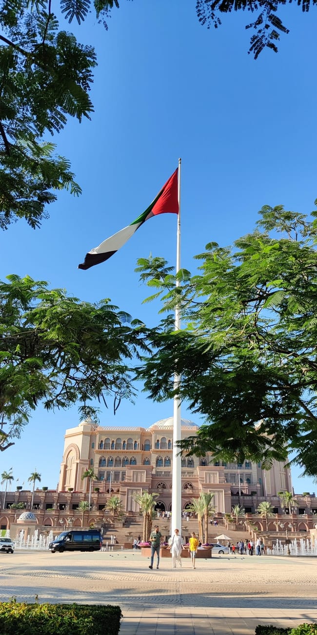 Emirates palace w abu zabi z flagą zea i palmami na pierwszym planie
