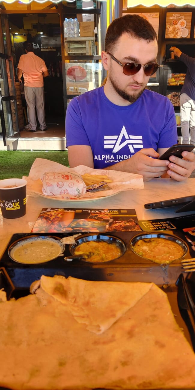 Punkt gastronomiczny abu dhabi foods z jedzeniem i napojami na stoliku oraz klientem w okularach przeciwsłonecznych.