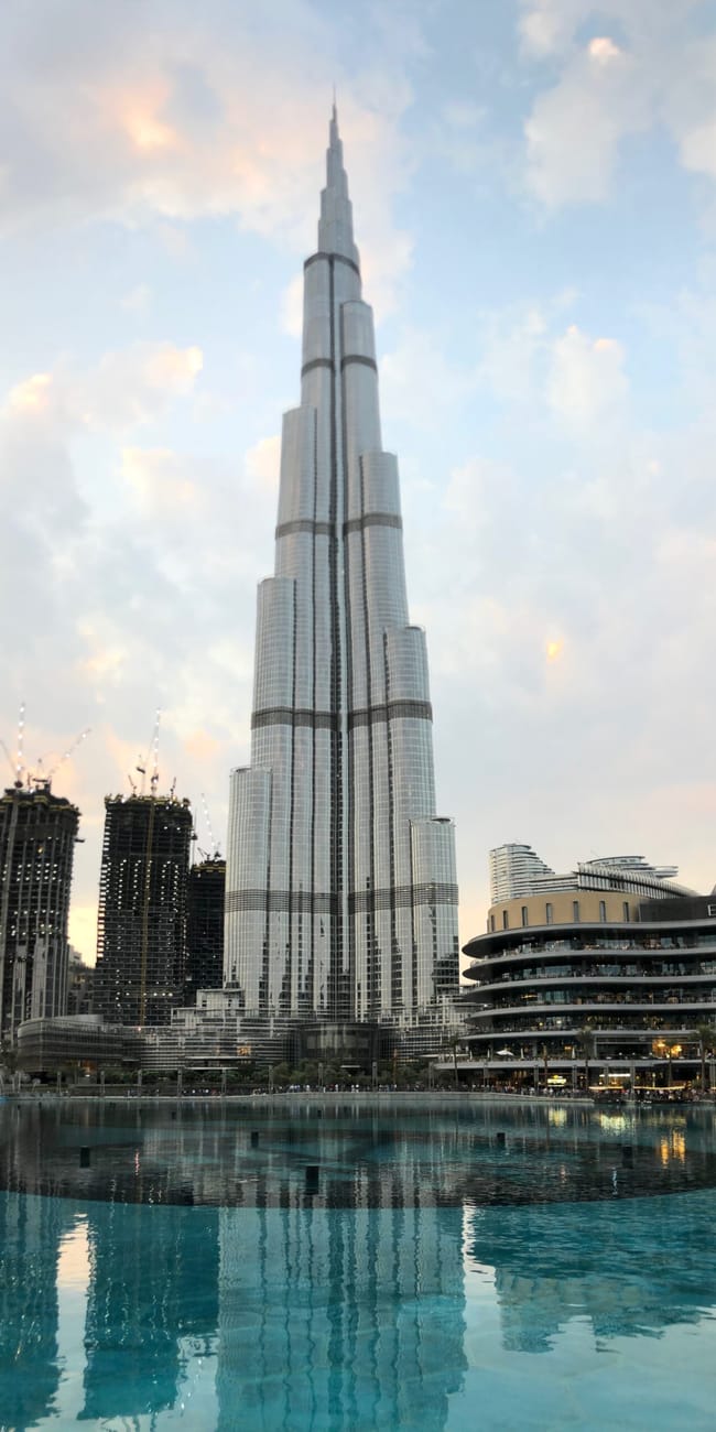 Burj khalifa w dubaju odbijający się w fontannie o zachodzie słońca