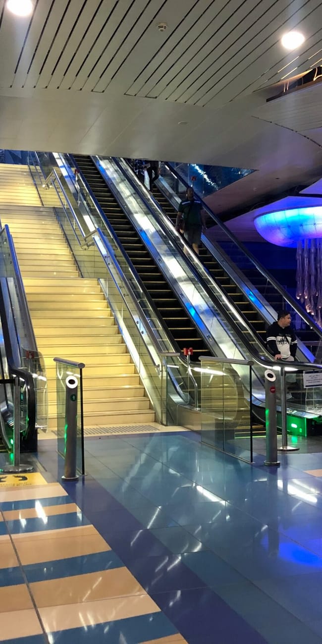 Wnętrze stacji dubai metro z ruchomymi schodami, neonowym oświetleniem i oznaczeniami wyjścia.