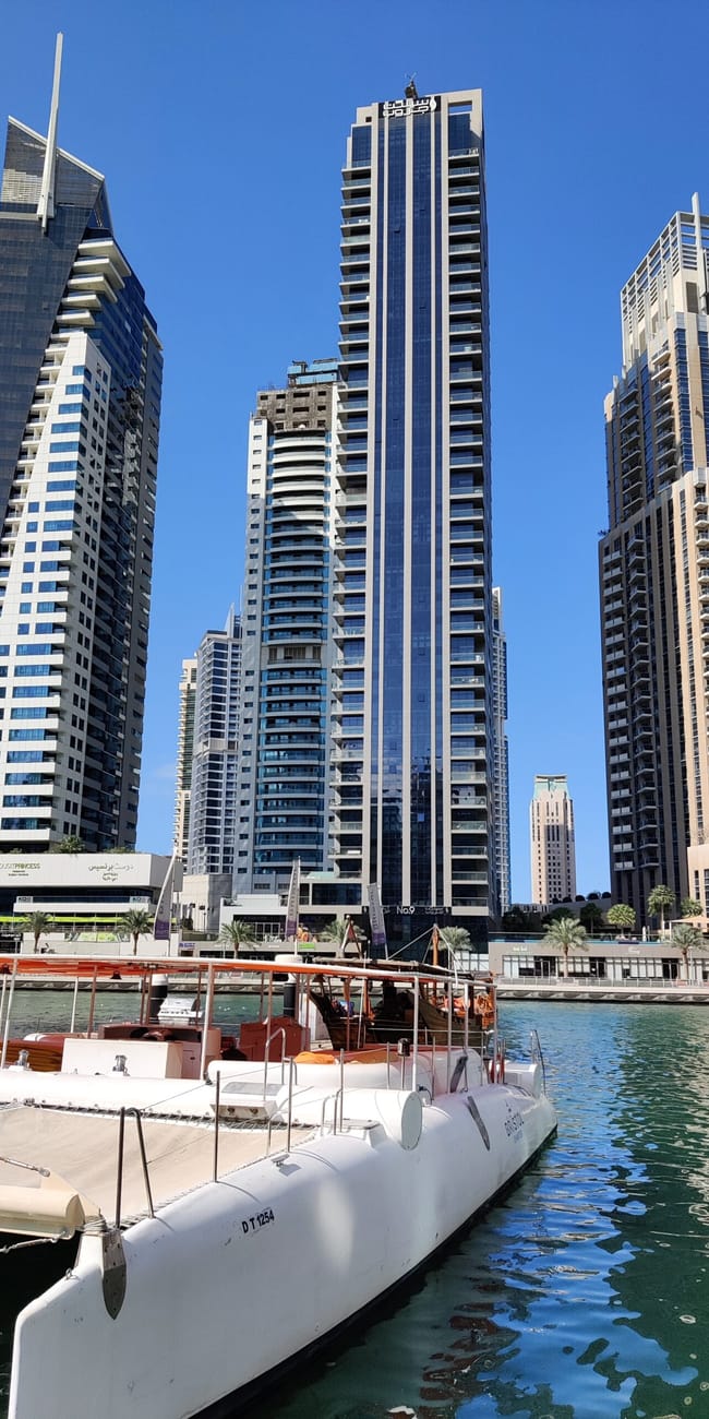 Dubai marina z nowoczesnymi wieżowcami i zacumowaną białą łodzią na wodzie