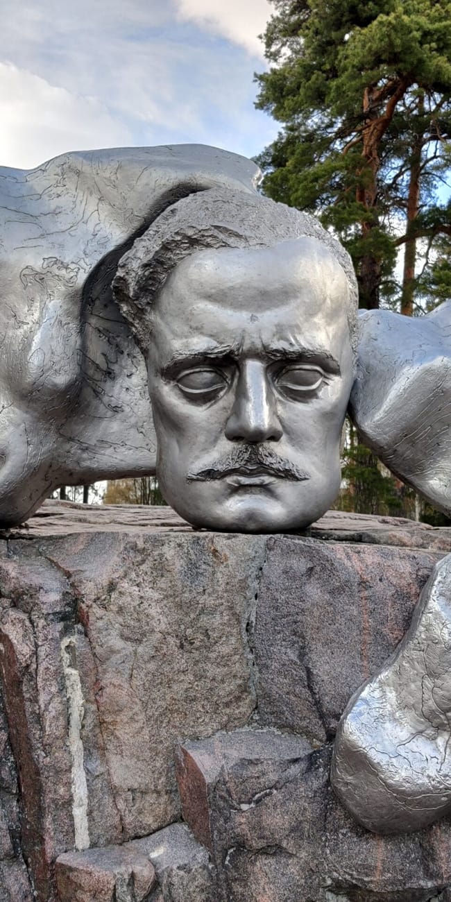 Pomnik sibeliusa w helsinkach z abstrakcyjną metalową rzeźbą na skałach, wśród drzew.