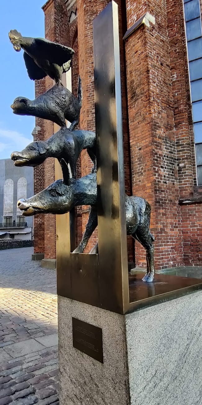 Rzeźba trzech braci na tle ceglanego budynku na starym mieście w rydze