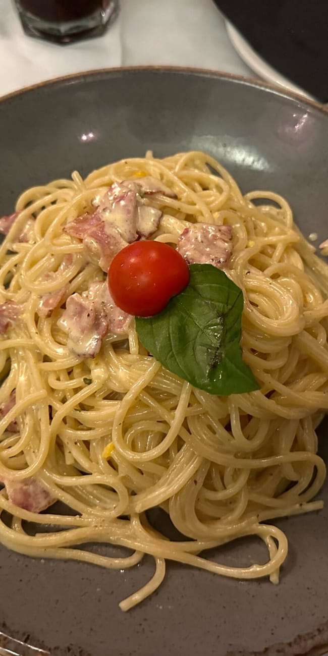 Spaghetti carbonara na talerzu w baden food, z pomidorkiem koktajlowym i listkiem bazylii.