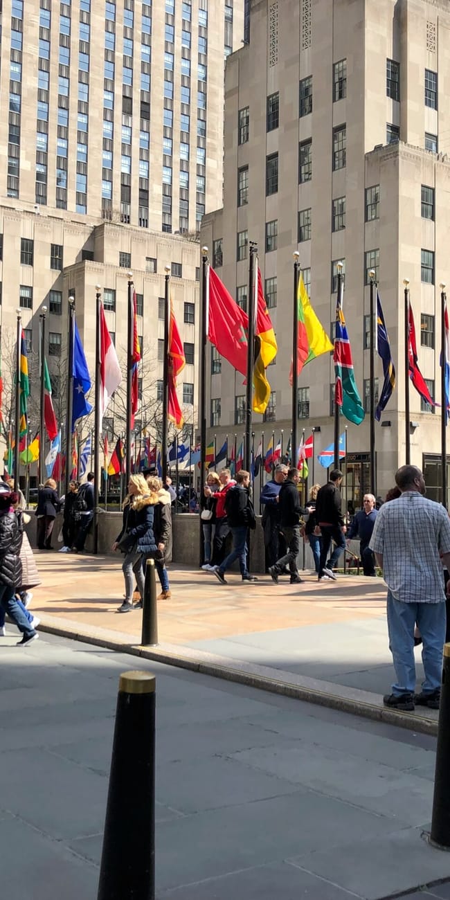 Rockefeller center w nowym jorku z szeregiem flag i spacerującymi ludźmi