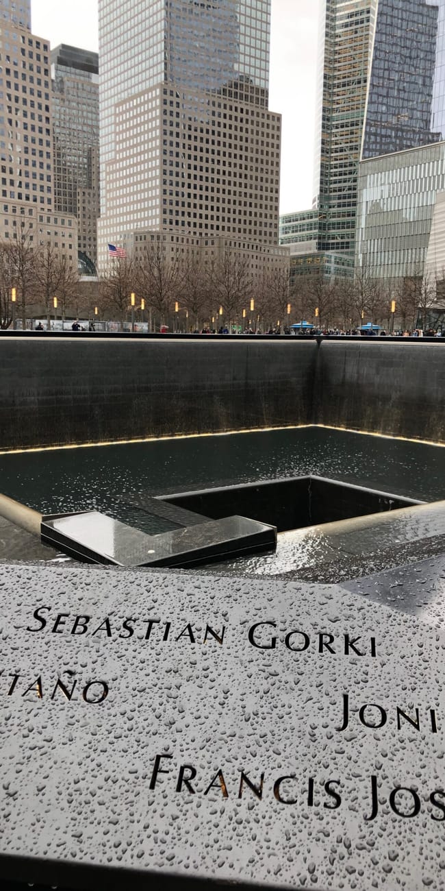 Memoriał 9/11 w nowym jorku z wodnym basenem i nazwiskami ofiar, otoczony wieżowcami.