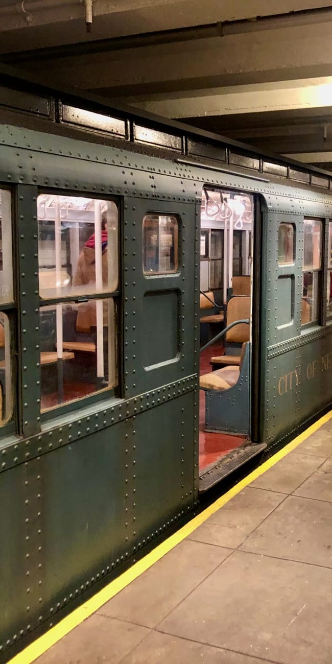 W new york transit museum stoi zabytkowy wagon metra z otwartymi drzwiami i drewnianymi siedzeniami.