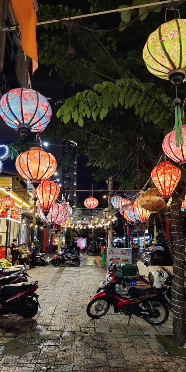 Nocna ulica w da nang ozdobiona kolorowymi lampionami i skuterami przy chodniku.