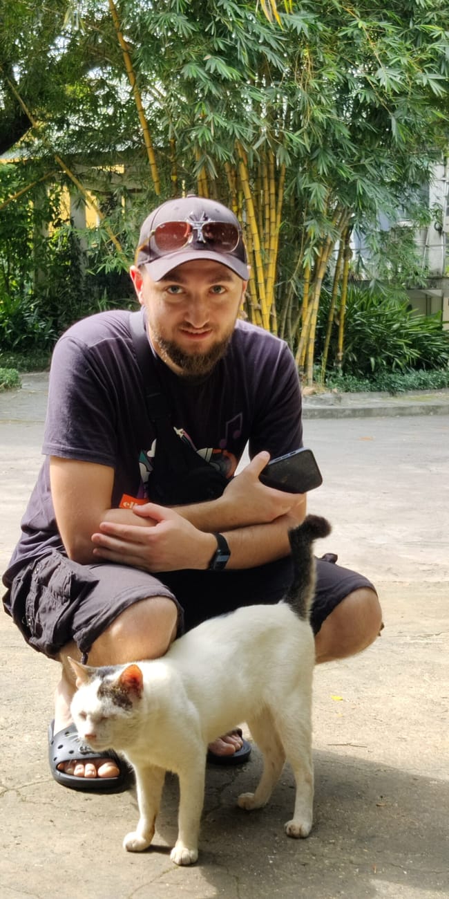 Mężczyzna kuca z białym kotem w ho chi minh zoo w wietnamie.
