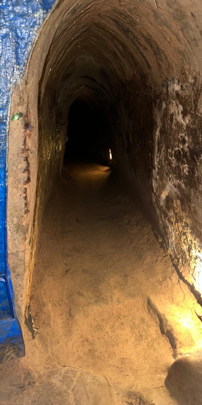 Wejście do tunelu cu chi w ho chi minh z wąskim, ciemnym korytarzem i oświetlonym ziemnym wejściem