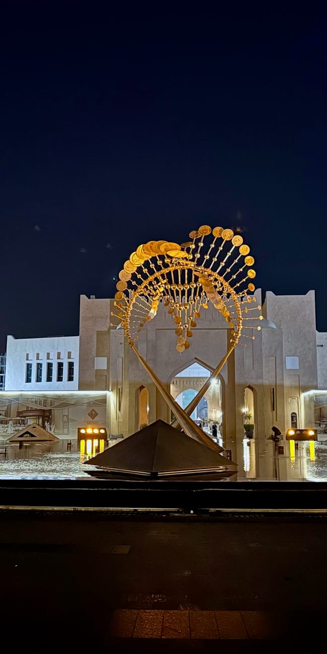 Katara cultural village w dosze nocą, z podświetloną złotą instalacją nad placem wodnym