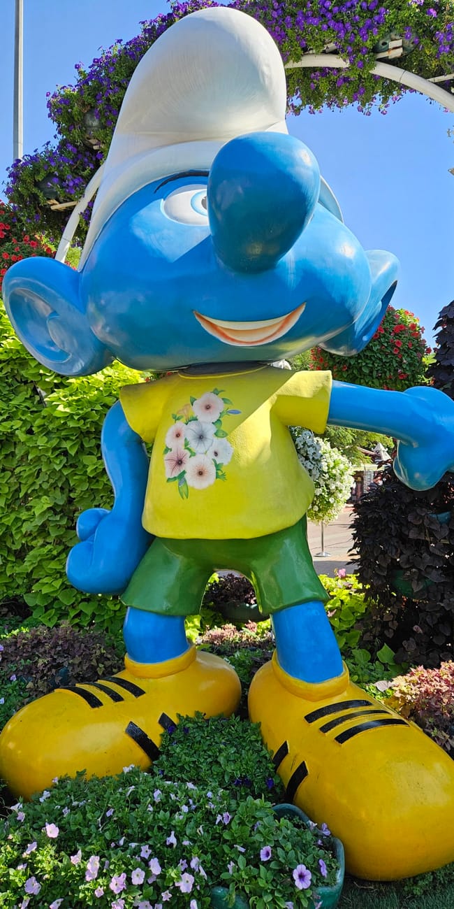 Dubai miracle garden: niebieski posąg smerfa wśród kolorowych kwiatów.