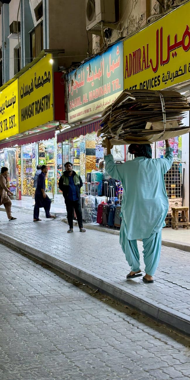 Sharjah al ghuwair market w nocy, z ulicznym sprzedawcą niosącym stertę kartonów.