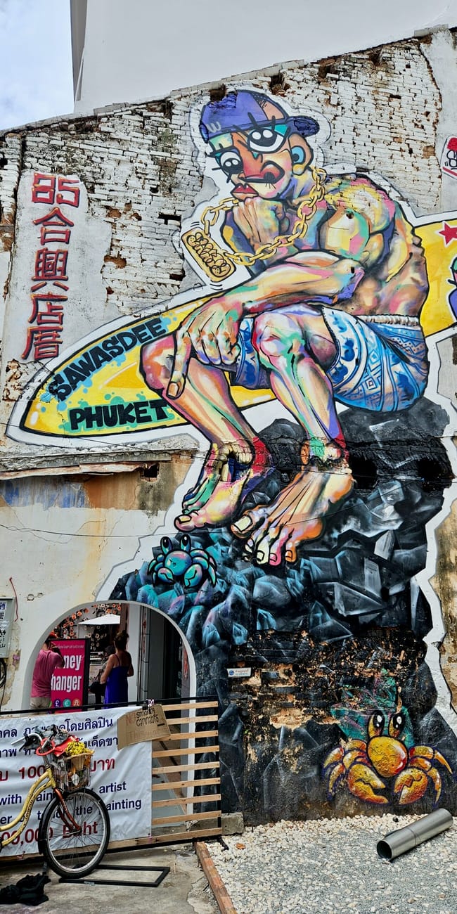 Mural street art w phuket, przedstawiający kolorową postać na zniszczonej ścianie budynku.