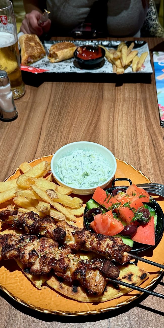 Posiłek w restauracji: szaszłyki z frytkami, sałatką i sosem, z piwem na stole.