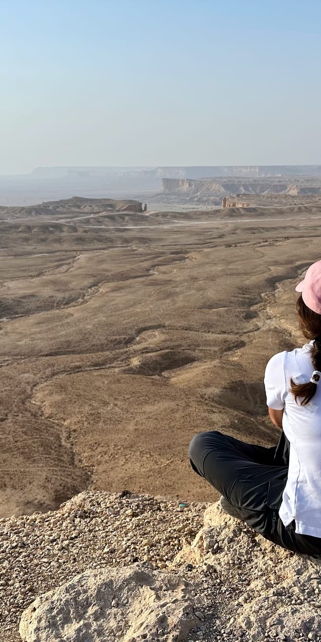 Woman sitting on a rocky overlook at edge of the world, saudi arabia, overlooking vast desert horizons